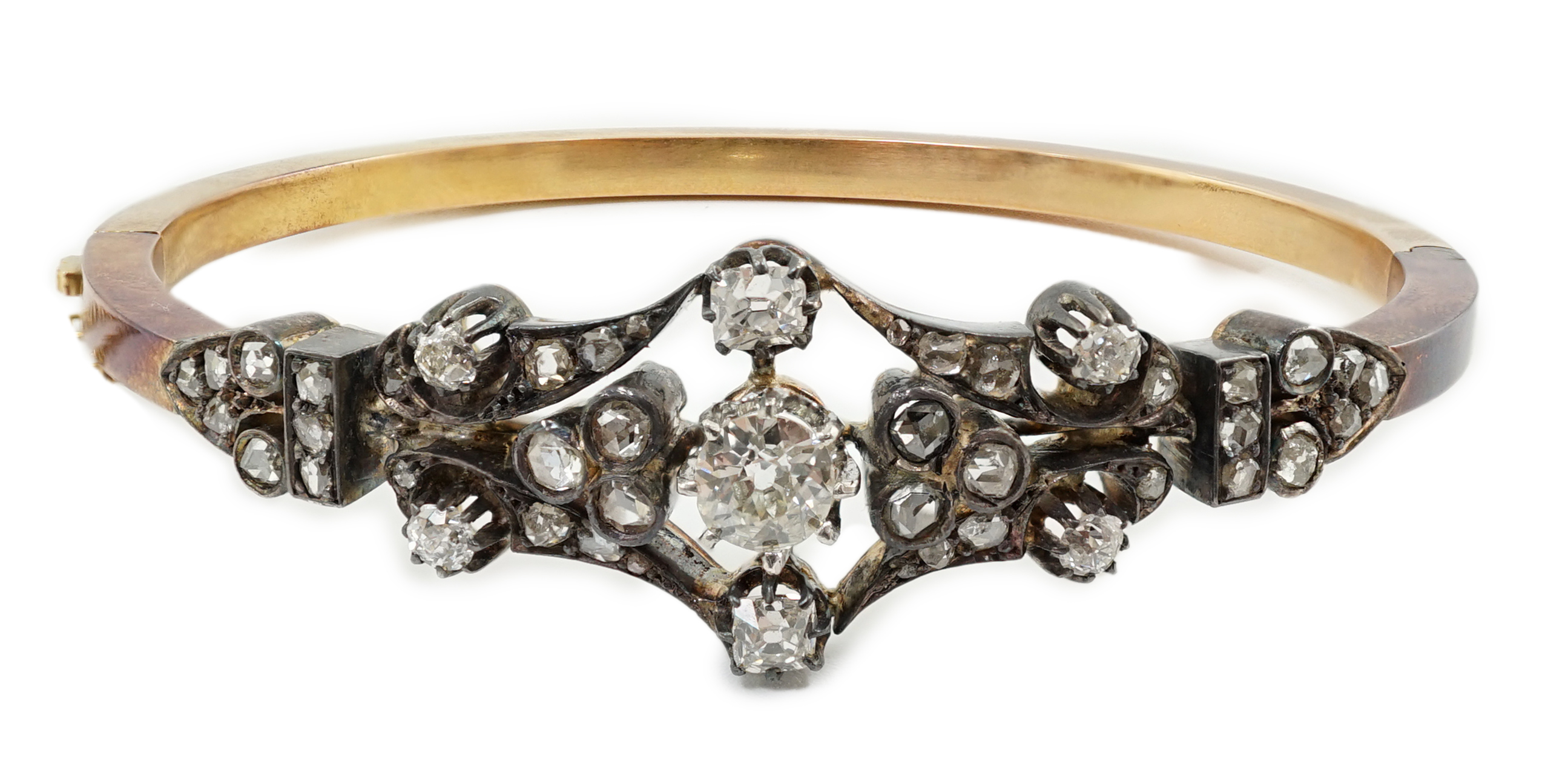 A late 19th/early 20th century French 18ct gold, silver, rose and round cut diamond cluster set hinged bangle